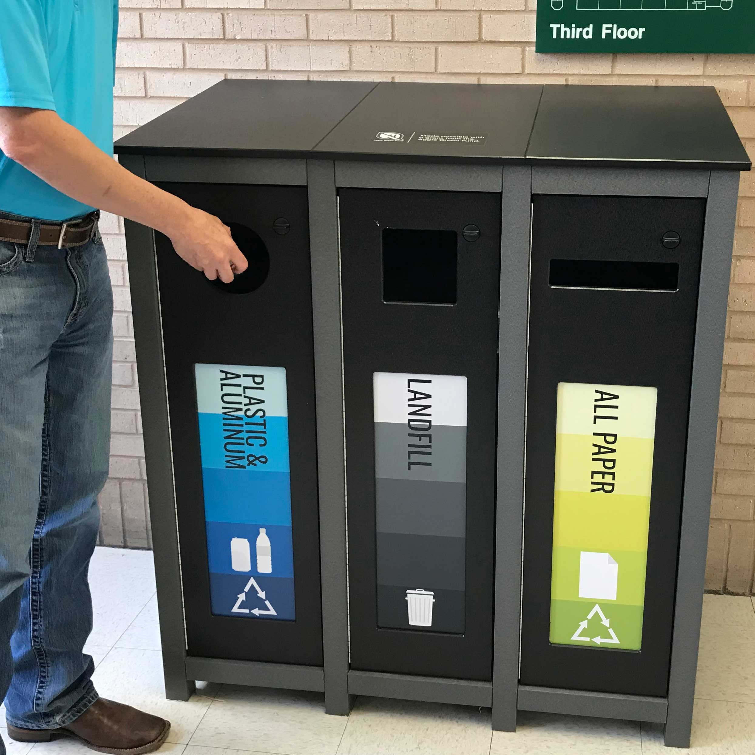 A person placing an item into a three-sectioned recycling bin.
